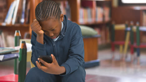 Unhappy-Young-Boy-Being-Cyberbullied-On-Mobile-Phone-In-School-Library